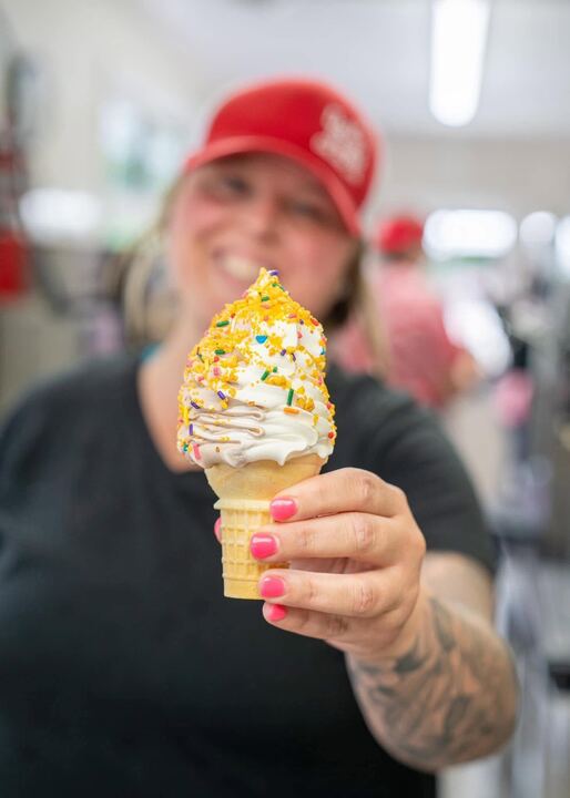 A smiling server holding out a sprinkle-dipped cone