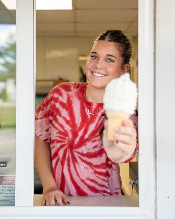 A crew member handing a vanilla cone out of the walk-up window