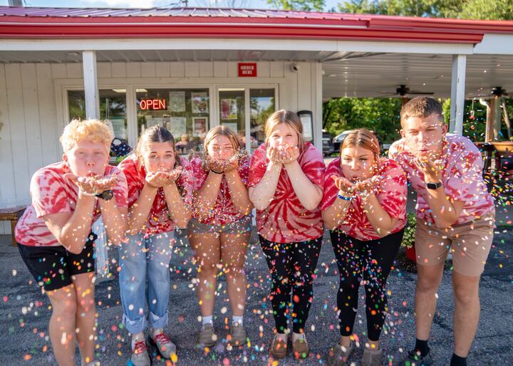 The Dairy Sweet crew in red tie-dye blowing confetti in front of the building