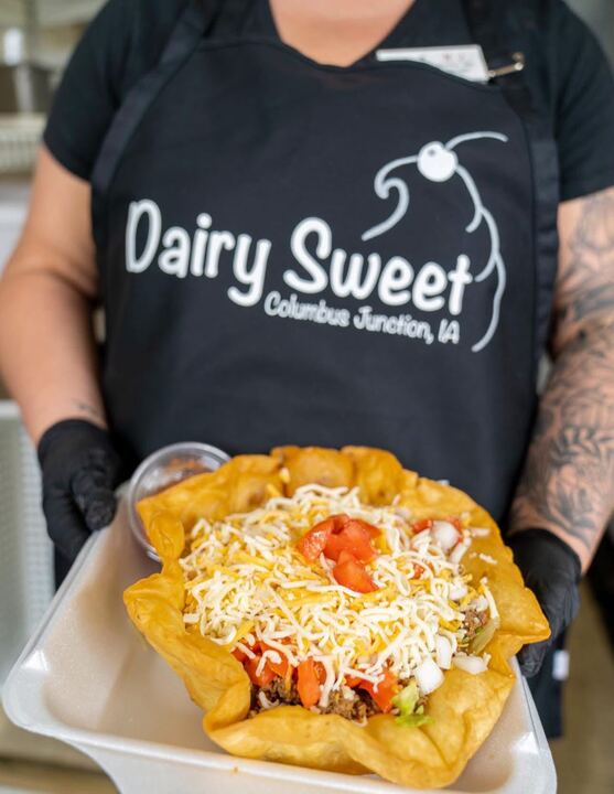 A taco salad in a crispy flour shell, held by a server in a Dairy Sweet apron