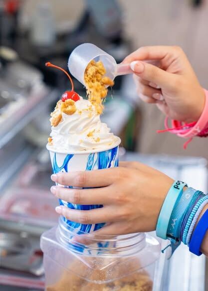 Toppings poured into a Spooner cup topped with whipped cream and a cherry