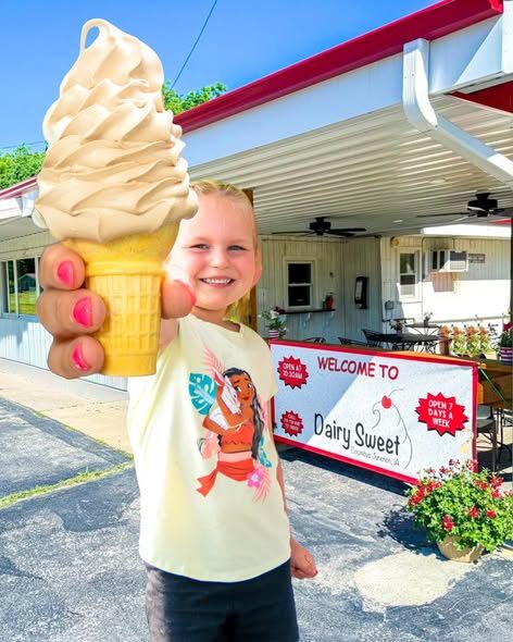 A little girl holding up a tall vanilla soft-serve cone in front of the Dairy Sweet