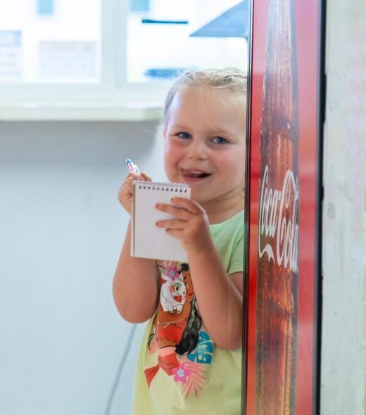 A little girl with a notepad pretending to take orders by the cooler